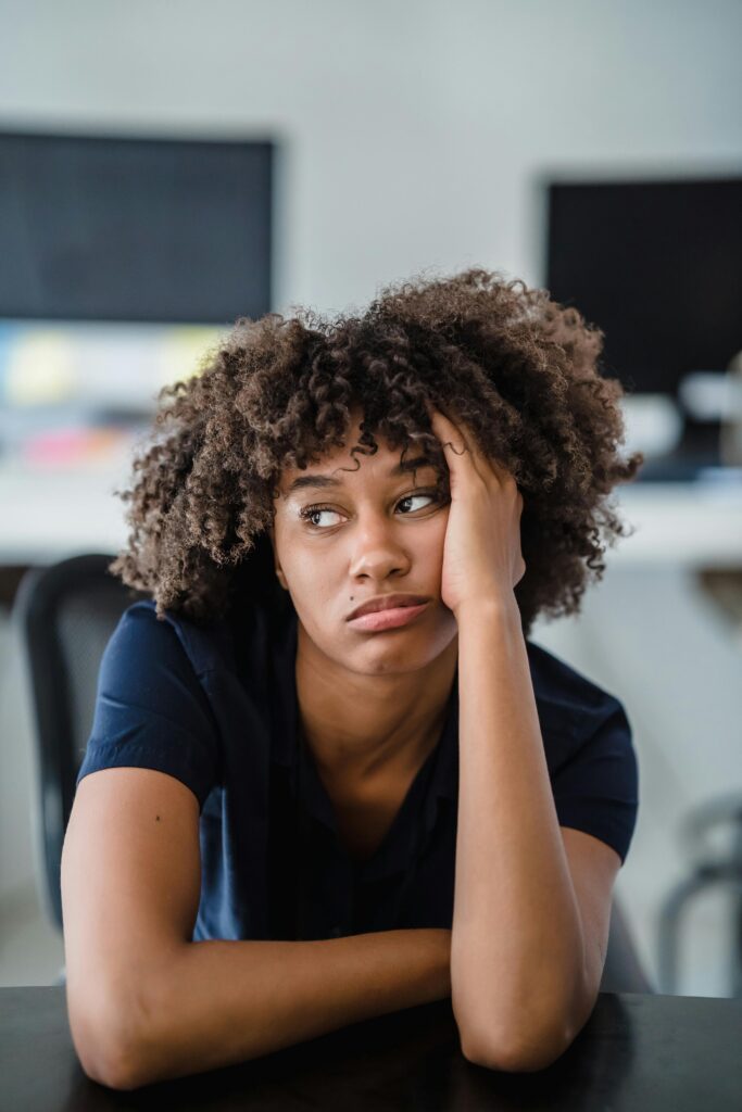 Portrait of a bored woman indoors, sitting with hand on face, expressing tiredness.