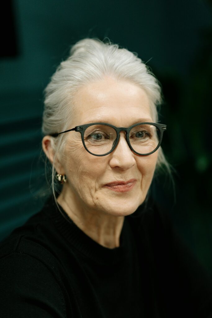 Sophisticated portrait of an elderly woman with white hair and eyeglasses, smiling gently.